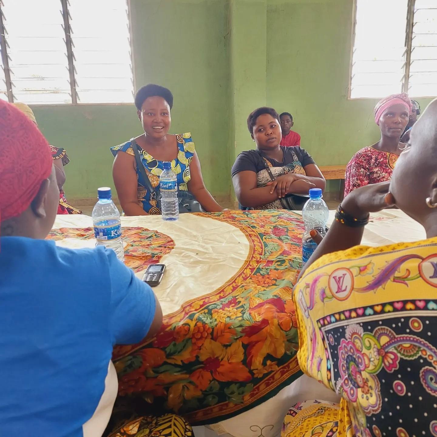Women sit around a table with a floral cloth during a group discussion, with water bottles and papers in front of them.
