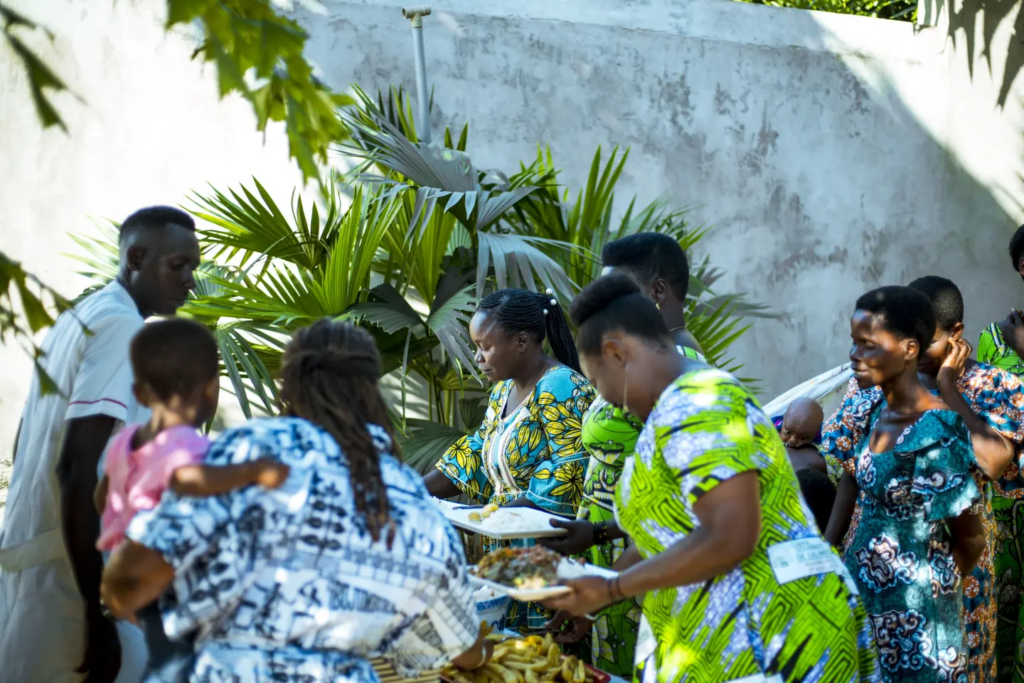 A group gathers outdoors around a table, with several people leaning toward it.