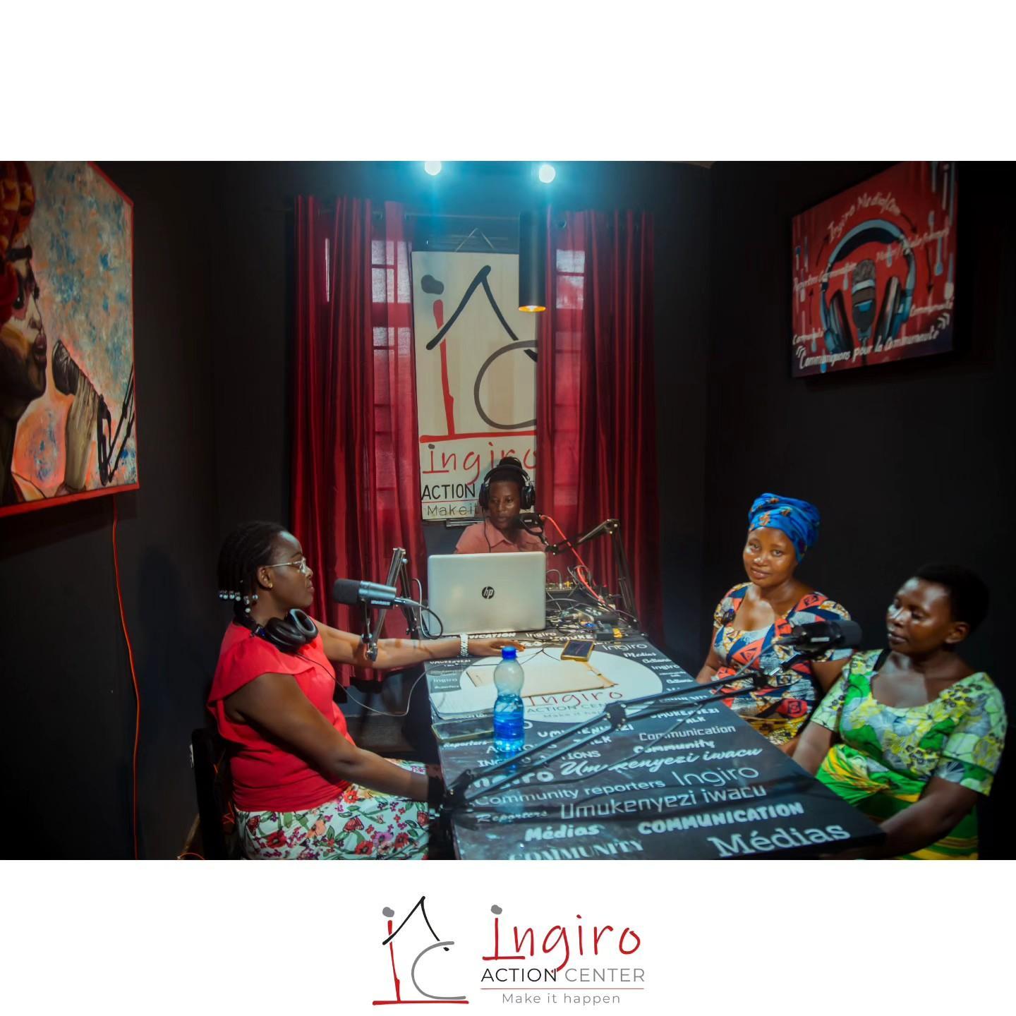 Several people sit around a table in a radio studio with microphones and audio equipment.