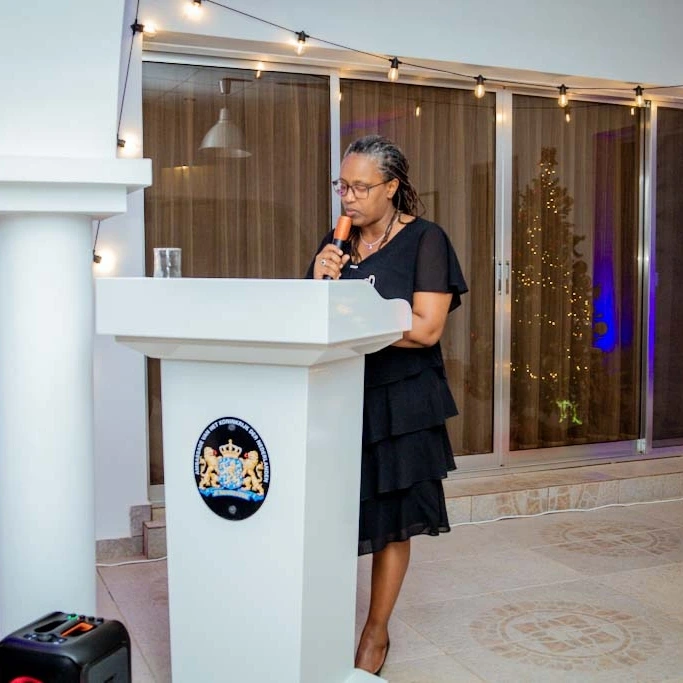A woman stands behind a lectern in a bright room with tall windows.