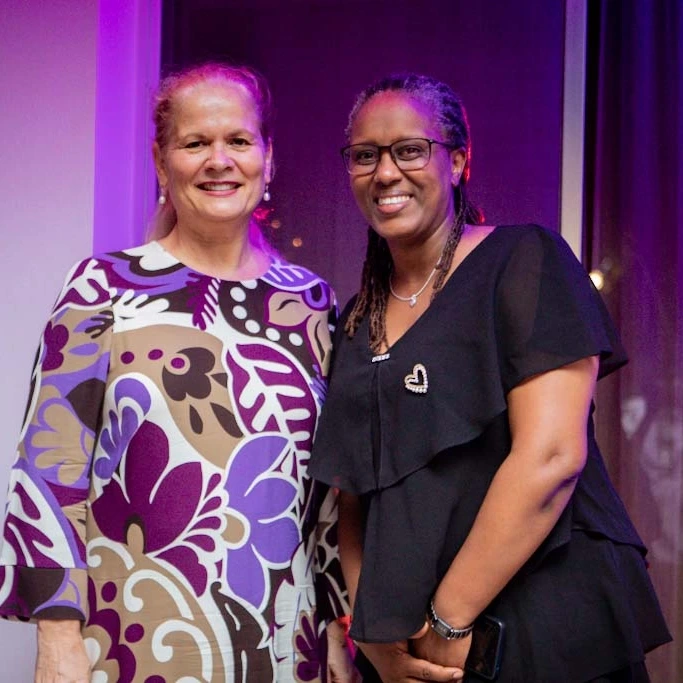 Two women stand side by side indoors and smile toward the camera.