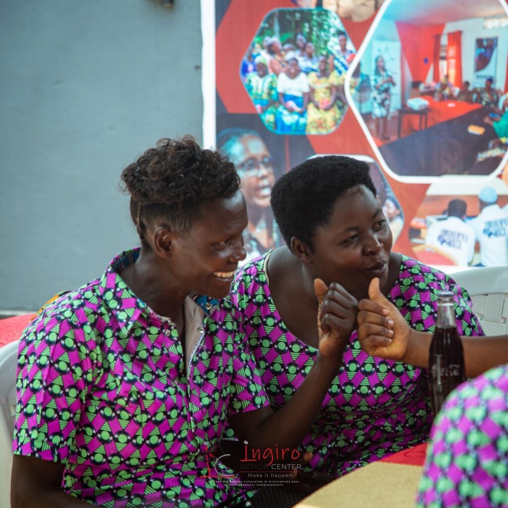 Two women in matching patterned clothing sit side by side and look toward each other.