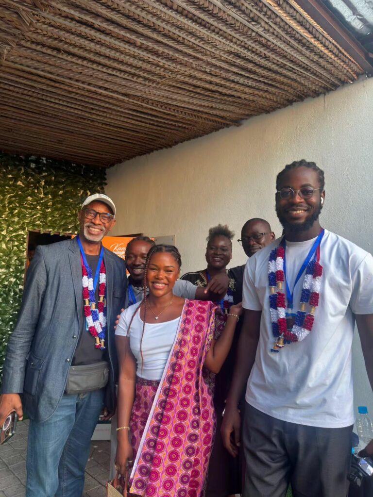 Five people pose together indoors, wearing event badges and lanyards.