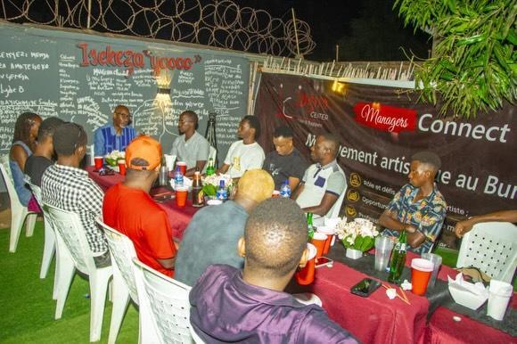 People sit together outdoors under lights beside a Managers Connect banner.
