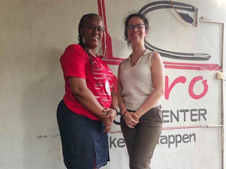 Two women stand together in front of a wall with an Ingiro Action Center sign.