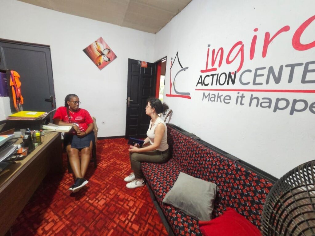 A person sits at a counter while another sits on a chair in an office with Ingiro signage.