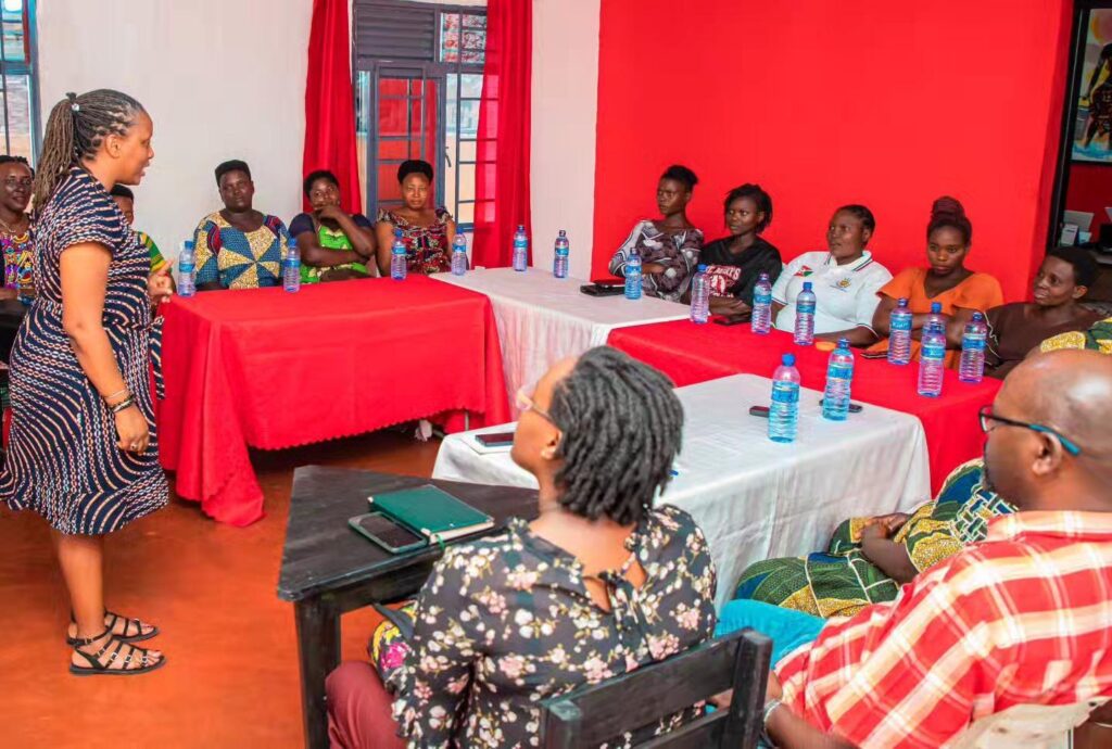 A person stands beside a table at the front of a meeting room as others sit facing them.
