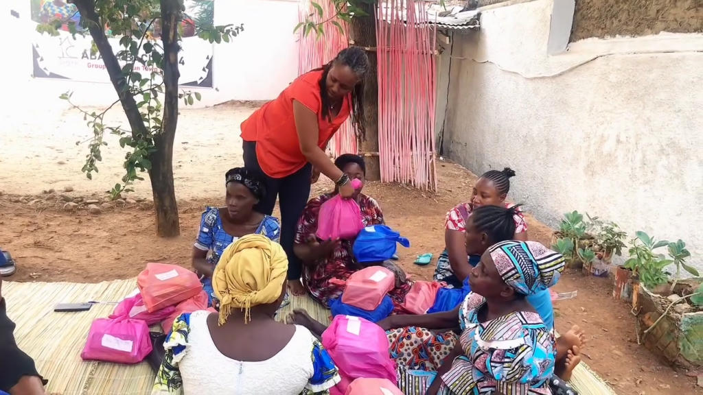 An adult in a red top leans toward children seated outdoors among colorful school bags.