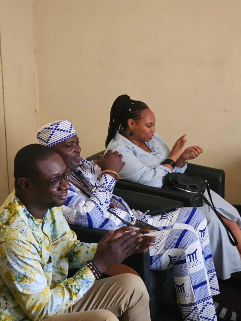 A woman gestures while seated among people in a meeting room.