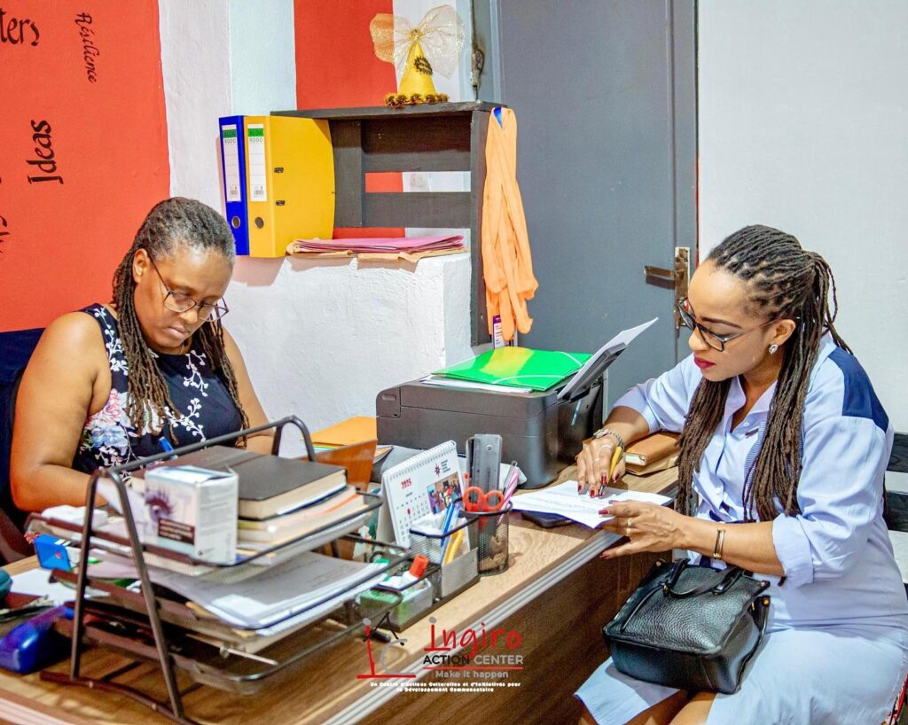 Two women sit across a desk with papers and folders between them.