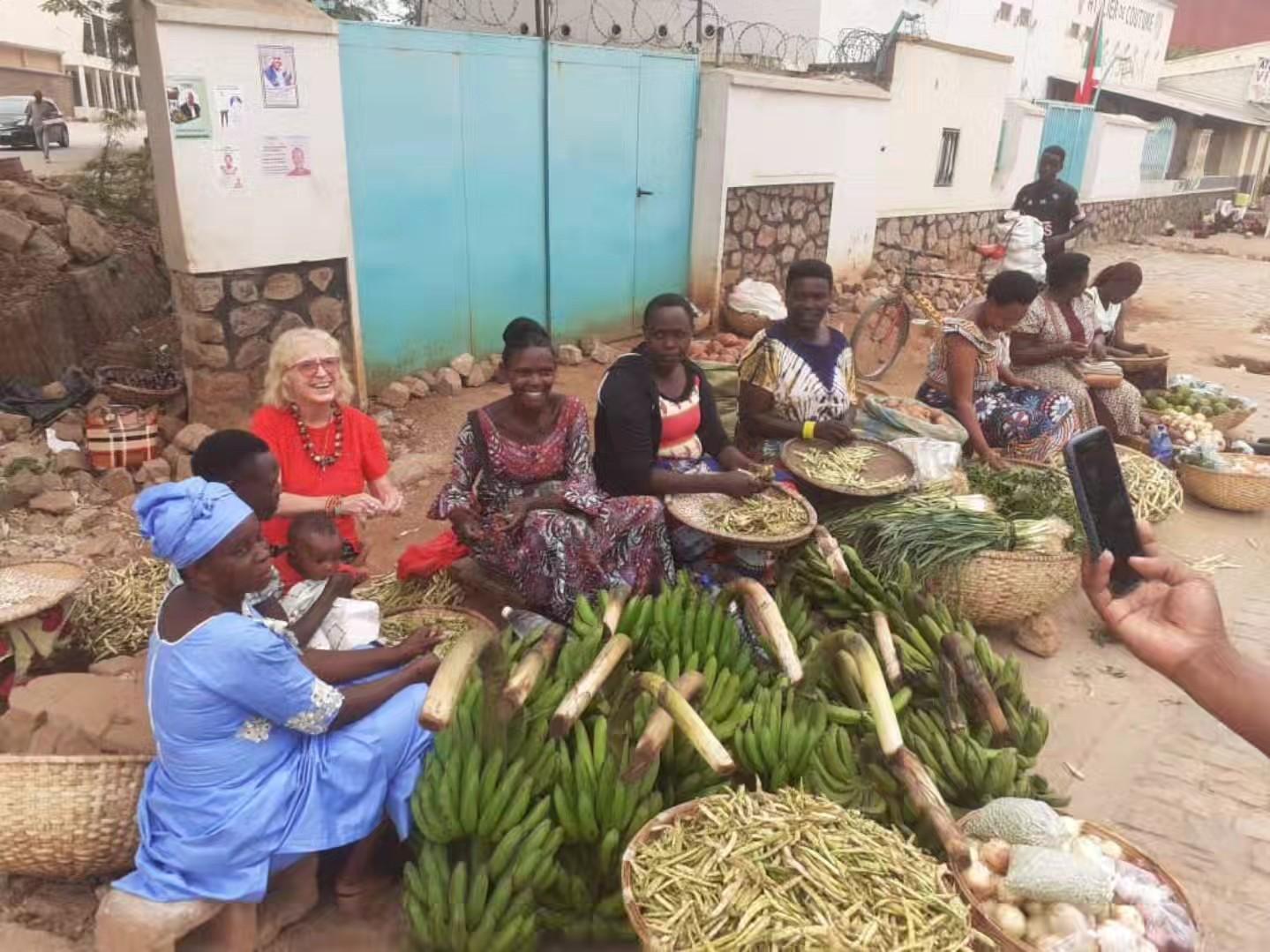 Several people sit together outdoors at a table with goods arranged in front of them.