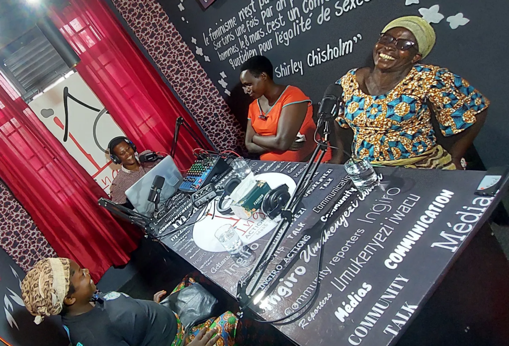 Several people sit around a studio table; one person gestures toward the group.