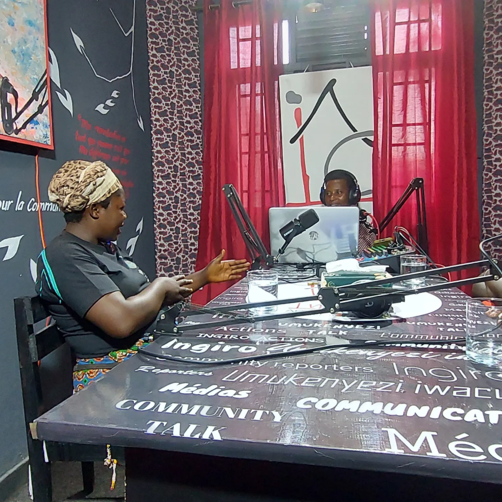 A small group gathers around a table in a radio studio with microphones.