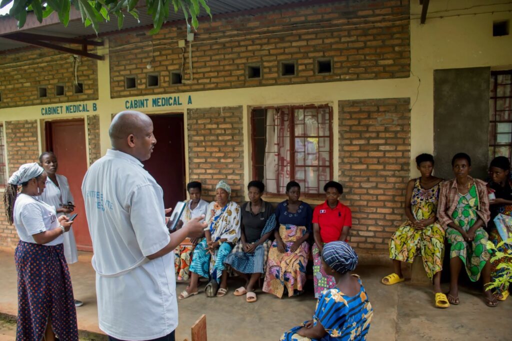 A man in a white shirt addresses women seated on benches outside consulting rooms marked Cabinet Médical A and B.