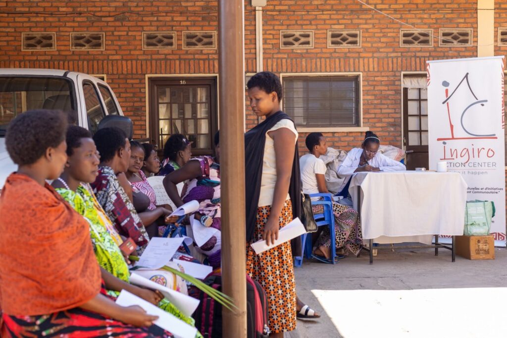 Women wait with papers in hand in front of a registration table and an Ingiro Action Center banner.
