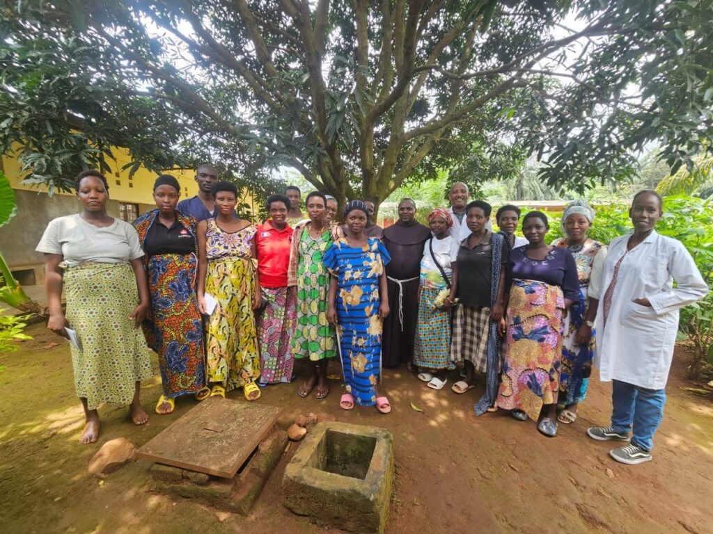A group of women stand together outdoors under a tree with a man in a white coat.