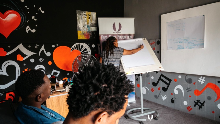 People sit in a brightly decorated room while a person writes on a whiteboard during a planning session.
