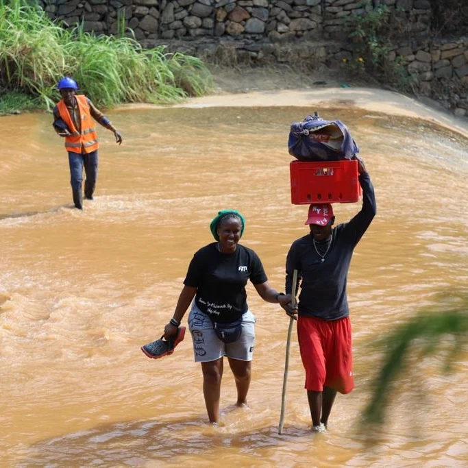 Crew members wade across a river, one carrying equipment on his head.