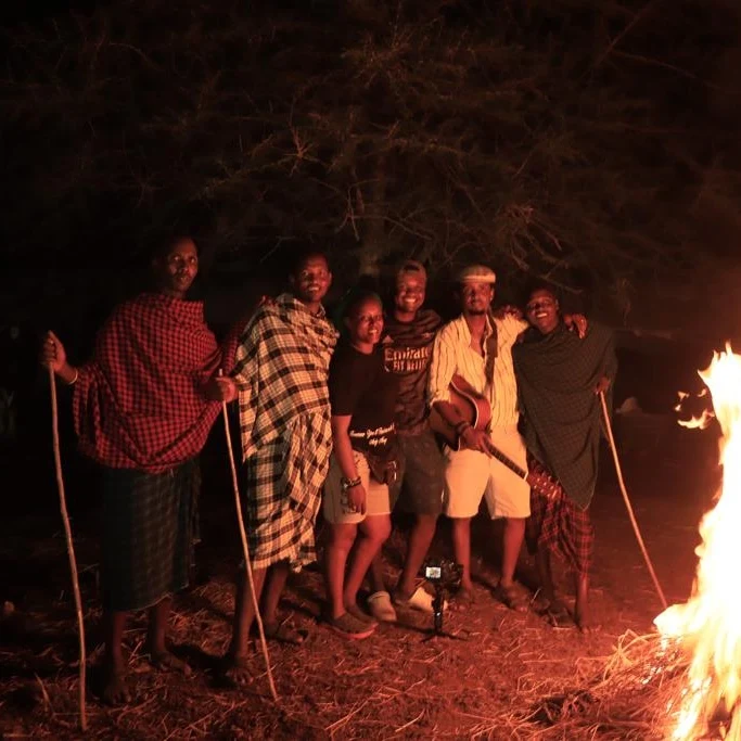 A group stands together at night beside a fire.